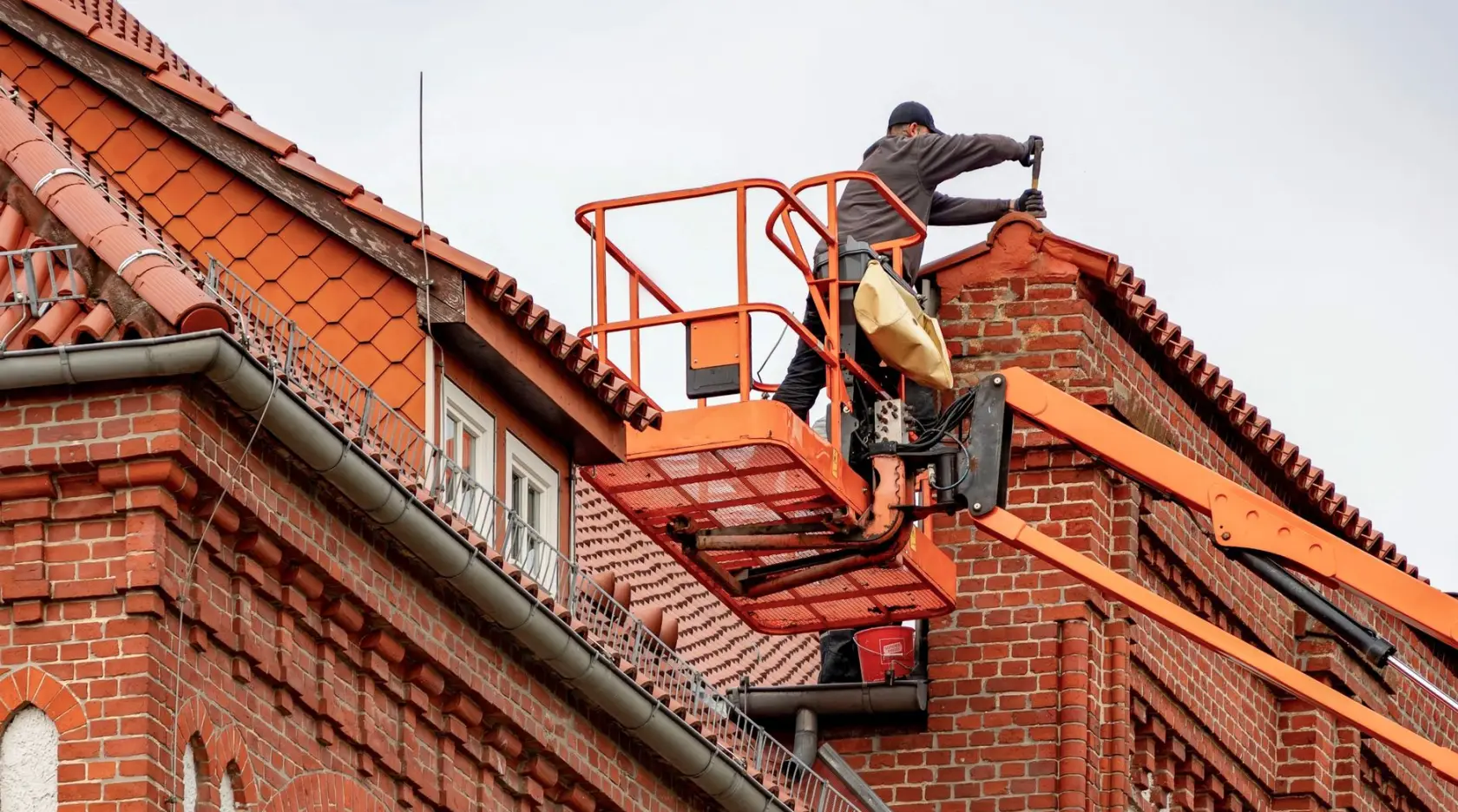 Roofer carrying out maintenance on a red brick building from a raised platform
